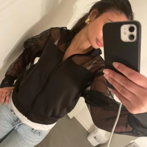 Svart jacka från Zara - Säljer en snygg svart jacka från Zara i storlek XS. Jackan har en cool design med genomskinliga mesh-ärmar och dragkedja framtill. Perfekt för en utekväll eller fest! 🖤