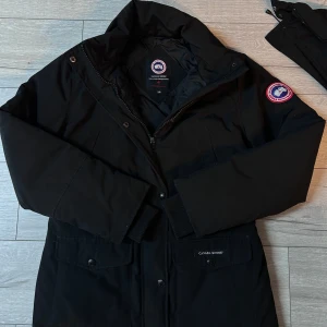 Svart parkajacka från Canada Goose - Säljer en svart parkajacka från Canada Goose med luva och dragkedja. Jackan har långa ärmar och en broderad logotyp på ärmen. Perfekt för kalla dagar. Skriv för mer info om de behövs👍
