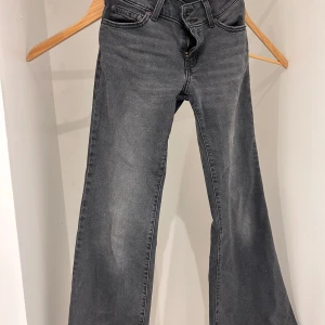 Grå Superlow Flare Jeans - Säljer ett par grå jeans i modellen Superlow Flare. De har en låg midja och en utsvängd stil som ger en retro känsla. Jeansen är i bra skick med en klassisk dragkedja och knapp framtill. Perfekta för en avslappnad look!
