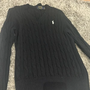 Svart stickad tröja från Polo Ralph Lauren - Säljer en snygg svart stickad tröja från Polo Ralph Lauren. Den har en klassisk v-ringning och det ikoniska logotypbroderiet på bröstet. Perfekt för både höst och vinter, med långa ärmar och ribbade muddar. Passar lika bra till vardags som till lite finare tillfällen.