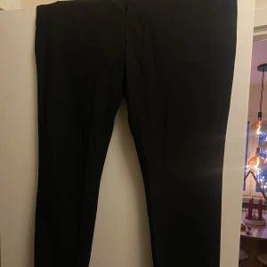 Svarta kostymbyxor från H&M - Snygga svarta kostymbyxor från H&M i slim fit. Perfekta för en stilren look. Byxorna har en klassisk design med en smal passform som ger en modern siluett.