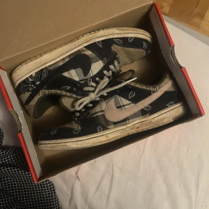 Nike Dunk med paisleymönster - Säljer ett par unika Nike Dunk sneakers med ett coolt paisleymönster i svart och beige. Skorna har en vintage look med slitna detaljer och snörning. Perfekta för dig som vill sticka ut med en retro stil!