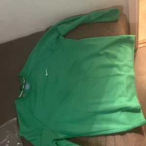 Grön tröja från Nike noocta  - Säljer en snygg grön tröja från Nike i bra skick. Den har en enkel design med en liten vit Nike-logga på bröstet. Perfekt för både vardag och träning. Passar bra till jeans eller träningsbyxor. Hör av dig vid intresse! Köpt är köpt tar ej emot tbx 