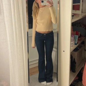 Stickad tröja  - Säljer en snygg beige/gul stickad tröja med långa ärmar och ribbade detaljer vid ärmslut och nederkant. Tröjan är jättemjuk och passar perfekt för en stilren look. Perfekt för kyligare dagar!