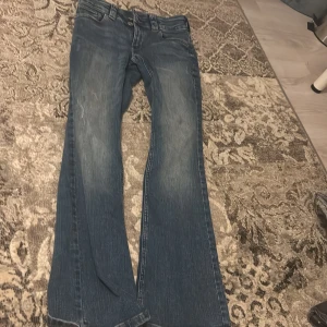 Blå bootcut jeans från H&M - Säljer ett par blå bootcut jeans från H&M. De har en låg midja och justerbar midja för perfekt passform. Perfekta för en avslappnad stil.