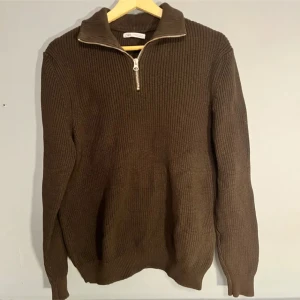 Brun stickad tröja från Zara - Snygg brun stickad tröja från Zara med dragkedja i halsen. Perfekt för kyliga dagar med sin ribbade design och långa ärmar. En stilren och bekväm tröja för alla tillfällen.
