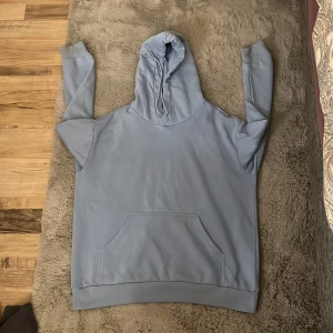 Ljusblå hoodie från H&M - Säljer en ljusblå hoodie från H&M i storlek M. Den är i bra skick och perfekt för både höst och vår. Hoodien har en stor ficka framtill och en bekväm huva. Materialet känns mjukt och skönt mot huden. Perfekt för en avslappnad stil! 💙