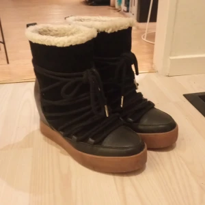 Svarta vinterboots med varmt foder - Säljer ett par svarta vinterboots i mycket bra skick. De har en snygg kombination av skinn och mocka med en varm, fluffig foderkant, invändigt också. De har snörning framtill och en inbyggd kilklack. Tålig gummisula som ger bra grepp. Perfekta för kalla vinterdagar, och kvällar ✨