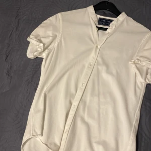 Vit kortärmad skjorta från Zara Man - Säljer en stilren vit kortärmad skjorta från Zara Man i storlek L. Skjortan har en modern design med knappar hela vägen och en enkel krage. Perfekt för både vardag och festliga tillfällen. Materialet känns lätt och bekvämt, vilket gör den idealisk för varmare dagar. Passar perfekt till jeans eller chinos!