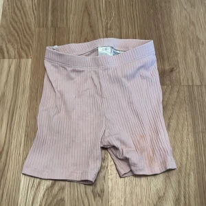 Rosa ribbade shorts från H&M - Säljer ett par söta rosa ribbade shorts från H&M i ekologisk bomull. Perfekta för varma sommardagar. De är mjuka och bekväma för de små att röra sig i. 🌸