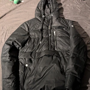 Svart pufferjacka från DreiMaster - Säljer en svart pufferjacka från DreiMaster med huva och dragkedja. Jackan har flera praktiska fickor och en stilren design, perfekt för kyligare dagar.