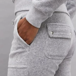 Juciy byxor - Säljer ett par grå mjukisbyxor med praktiska fickor och snygga sömdetaljer. Perfekta för en avslappnad stil och bekväma att bära hela dagen. Dock lite uppklippta och lite slutet material