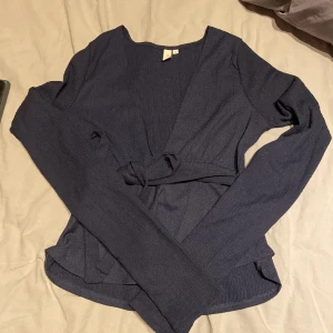 Mörkblå ribbad topp från Nelly - Säljer en stilren mörkblå ribbad topp från Nelly. Toppen har långa ärmar och en knytning i midjan som ger en snygg passform. Perfekt för både vardag och lite finare tillfällen.