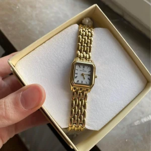 Guldfärgad klocka från Mockberg - Elegant guldfärgad klocka från Mockberg med rektangulär urtavla och romerska siffror. Armbandet är i metall med en klassisk länkdesign. Perfekt för en stilren look.