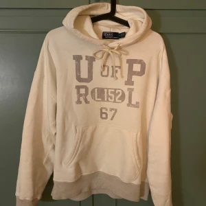 Beige hoodie från Polo Ralph Lauren - Säljer en snygg beige hoodie från Polo Ralph Lauren med tryck på framsidan.  Nypris ligger på ungefär 2500kr och mitt pris är 1300kr Priset kan diskuteras vid snabb affär.