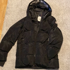 Svart dunjacka från Moncler - Säljer en snygg svart dunjacka från Moncler i mycket bra skick. Jackan har en huva med Moncler-logga och dragkedja framtill. Perfekt för kalla vinterdagar. Den har långa ärmar och är supervarm och bekväm. Passar både till vardags och lite finare tillfällen.