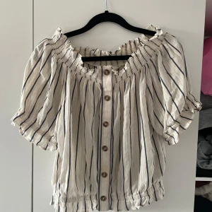 Randig of-shoulder topp/blus - En beige aktig of shoulder top med räfflat material vid armarna och magen med knappar i mitten. Supersnygg till Lågmidjade jeans!