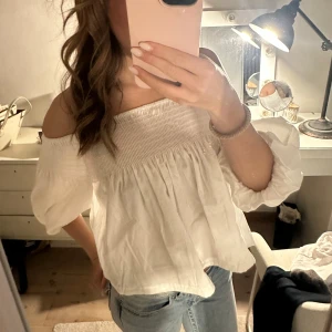 Vit offshoulder blus - Säljer en söt vit offshoulder blus med trekvartsärm och smockdetaljer upptill. Knappt använd och inga fläckar. 
