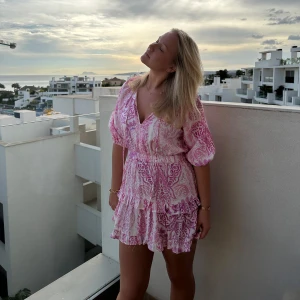 Rosa mönstrad klänning - Charmig rosa klänning med blommigt mönster och volangdetaljer. Klänningen har en v-ringad hals och trekvartsärmar, perfekt för sommarens festligheter.💕 Endast använder 2 gånger (dom på bilden) Säljer då den är för kort på mig💕 (178 cm lång) 