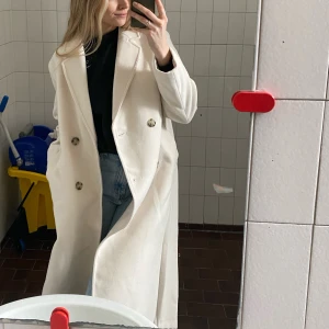 Crémevit lång kappa - Stilren vit kappa köpt från H&M, den har använts några fåtal gånger. Inga fläckar, inget slitage, precis som ny. köptes för 599, säljer för 349
