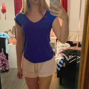 Blå v-ringad t-shirt - Säljer en enkel blå t-shirt med v-ringning. T-shirten har korta ärmar och är gjord i ett mjukt material. Från märket Anna field!