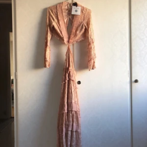 Rosa spetsklänning från My Eye - Säljer en superfin rosa långklänning i spets från My Eye. Klänningen har långa ärmar och en djup v-ringning. Den är dekorerad med volanger och har knappar i ryggen. Perfekt för fest eller bal! 💖