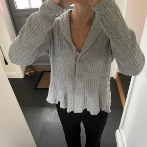 Grå stickad kofta  - Grå kofta med volanger från Mywear i storlek M, skulle säga att den även passar S. Fint skick. Använd gärna köp nu!