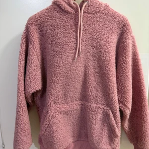 Rosa fleece hoodie - Mysig rosa fleece hoodie perfekt för kyliga dagar. Den har en stor huva och en praktisk ficka framtill. Perfekt för att hålla sig varm och bekväm under höst och vinter. Passar både för hemmamys och utomhusaktiviteter.