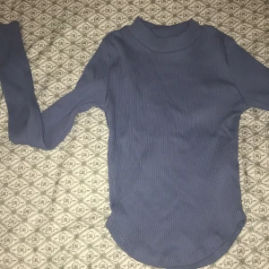 Blå ribbad polotröja - Säljer en snygg blå ribbad polotröja i mycket bra skick. Perfekt för höst och vinter med sin långa ärmar och sköna passform. Tröjan är både stilren och bekväm, idealisk för lager-på-lager eller som den är. Passar perfekt till jeans eller kjol!