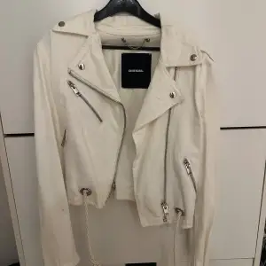 Säljer en snygg vit jacka från Diesel. Den har en cool bikerstil med dragkedjor och knappar i silver. Jackan är långärmad och har en croppad passform med snörning i nederkant. Perfekt för att ge din outfit en edgy touch! Använd 1 gång. Nypris är 1799