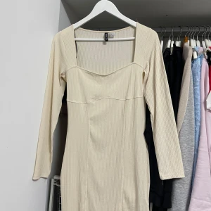 Beige ribbad klänning från Divided - Säljer en superfin beige klänning från Divided. Den är ribbad och har en snygg fyrkantig urringning. Klänningen är långärmad och har en tight passform som framhäver figuren. Perfekt för både vardag och fest! Endast använts en enda gång.