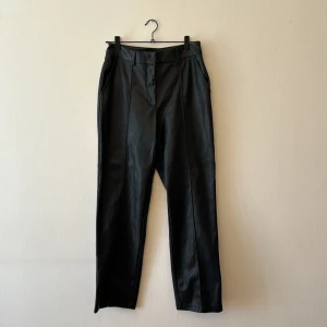 Svarta skinnbyxor - Säljer ett par snygga svarta skinnbyxor i högmidjad modell. De har en rak passform och stilrena detaljer med fickor både fram och bak. Perfekta för en cool och elegant look!