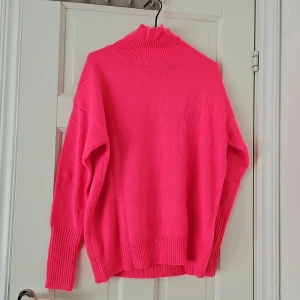 Neonrosa stickad polotröja - Säljer en supercool neonrosa stickad polotröja. Den är perfekt för att lysa upp vilken grå dag som helst! Tröjan har långa ärmar och en hög polokrage som håller dig varm och mysig. Perfekt för höst och vinter. Oanvänd