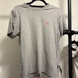 Grå t-shirt från Dickies - Säljer en klassisk grå t-shirt från Dickies med en liten logga på bröstet. T-shirten har en normal passform och är tillverkad i mjukt bomullsmaterial. 