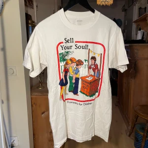 Vit t-shirt med tryck - Vit t-shirt med ett humoristiskt tryck som säger 'Sell Your Soul! Economics for Children'. Den har en färgglad illustration på framsidan. Perfekt för den som gillar unika och roliga plagg.