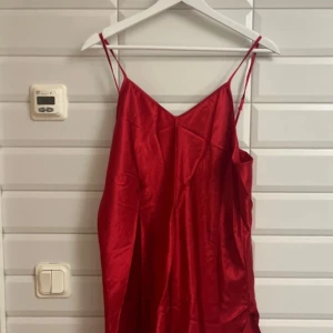 Röd axelbandslös klänning/pyjamas  - Snygg röd klänning i satin med smala axelband och en elegant v-ringning. Perfekt för en kväll ute eller en speciell tillställning. Den har en lätt och flödande passform som ger en feminin silhuett. Aldrig använd. Storlek:XL. Jag säljer för 100 kronor. ✨