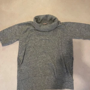 Grå polotröja från Kappahl  - Säljer en mysig grå polotröja från Kappahl. Tröjan har en hög polokrage och trekvartsärmar, perfekt för kyliga dagar. Den är tillverkad i ett mjukt material som känns skönt mot huden. Passar bra till både jeans och kjol.