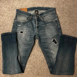 Blå jeans från Dondup - Snygga blå jeans med skön tvätt från Dondup med slitna detaljer och hål för en trendig look. De har en klassisk femficksdesign och knappgylf. Perfekta för en avslappnad stil. Riktigt bra skick! Storlek 30! Hör av er vid minsta lilla!😊