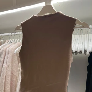 Beige ärmlös topp från Zara - Säljer en stilren beige ärmlös topp från Zara. Perfekt för lager-på-lager eller att bära som den är. Toppen har en mjuk och bekväm passform.