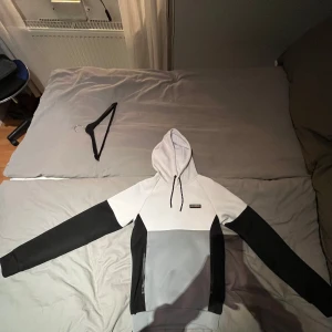 Grå och vit hoodie med matchande byxor - Säljer en stilren grå och vit hoodie med svarta detaljer och matchande byxor. Hoodien har en praktisk dragkedja och en bekväm passform. Perfekt för en avslappnad look.