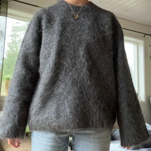 Grå stickad Alpaca Tröja - Säljer en mysig grå tröja med fluffig textur. Tröjan har en enkel design med långa ärmar och en rund hals. Perfekt för kyliga dagar när du vill ha något bekvämt och stilrent. Passar bra till jeans eller leggings. Liknar den från toteme, Ny med prislapp och endast testad! Väldigt eftertraktad och slut på hemsidan🥰