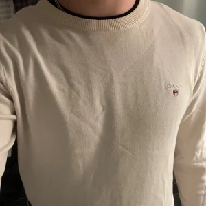 Vit tröja från GANT - Tjena, säljer en stilren benvit tröja från GANT i bomull. Tröjan har en rund halsringning och ett diskret broderat GANT-emblem på bröstet. Perfekt för en avslappnad och snygg look. Fint skick utan fläckar eller andra defekter. Passar både över skjortan eller t-shirten😁Tröjan är i storlek S men passar även XS. Hör av dig vid frågor eller funderingar👍🏼