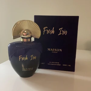 Fresh Iris Eau de Parfum från Maison Asrar - Elegant parfymflaska i mörkblått med guldtext och en unik guldfärgad kork. Flaskan rymmer 100 ml av doften Fresh Iris. Förpackningen är stilren och matchar flaskans design.