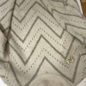 Beige stickad tröja från Kappahl - Säljer en beige stickad tröja från Kappahl med ett snyggt zickzack-mönster i silver. Tröjan har långa ärmar och ribbstickade muddar vid ärmslut och nederkant. Perfekt för kyliga dagar! ✨