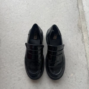 Svarta loafers från Zara - Snygga svarta loafers från Zara i en glansig finish. Skorna har en klassisk design med rundad tå och en robust sula för extra komfort. Väl använda, skick enligt bilder.