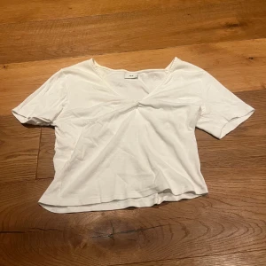 Vit kortärmad topp från JDY - Säljer en stilren vit topp från JDY i storlek S. Toppen har korta ärmar och en subtil v-ringning med en liten knutdetalj framtill. Perfekt för en enkel och fräsch look.