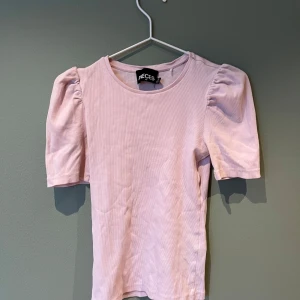 Ljusrosa ribbad topp från Pieces - Säljer en söt ljusrosa ribbad topp från Pieces med korta puffärmar. Perfekt för en avslappnad och stilren look. Toppen har en rund halsringning och är gjord i ett mjukt material.💕