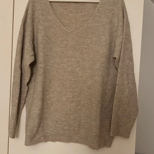 Beige stickad tröja från 157 - Säljer en stilren beige stickad tröja från 157. Tröjan har en v-ringad hals och långa ärmar, perfekt för kyligare dagar. Den är mjuk och bekväm, idealisk för både vardag och avslappnade tillfällen.