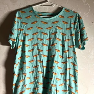 Turkos t-shirt med korvmönster från Biltema - Cool turkos t-shirt från Biltema med ett roligt korvmönster över hela tyget. Perfekt för dig som vill sticka ut med en unik stil.