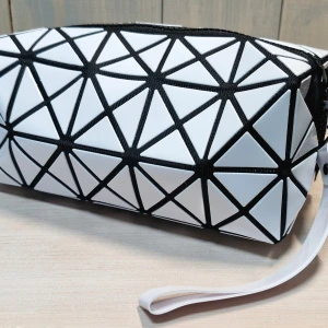 Vit geometrisk handväska - Snygg vit handväska med ett unikt geometriskt mönster i svart. Väskan har en praktisk dragkedja och ett bekvämt handtag för enkel bärning. Perfekt för att ge din outfit en modern touch.